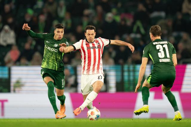 SC Freiburg midfielder Nicolas Höfler competes for possession with VfL Wolfsburg players Adam Daghim and Yannick Gerhardt, 20. December 2025.
