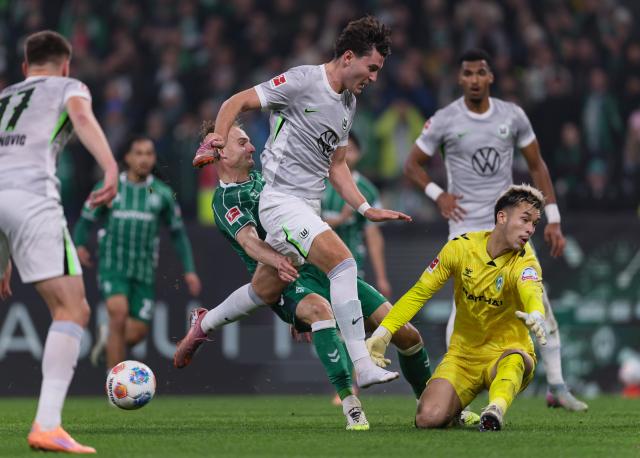 VfL Wolfsburg striker Jonas Wind attempts a shot while holding his left boot in his right hand, 7. November 2025.