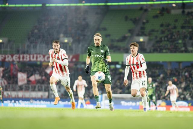 VfL Wolfsburg attacking midfielder Lovro Majer contests for possession with two SC Freiburg players, 20. December 2025.